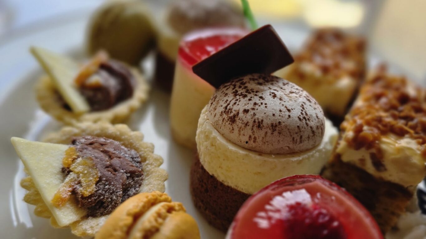 A plate with an assortment of small pastries and desserts, including macarons, tarts, cakes, and mousse, arranged in a close-up view.