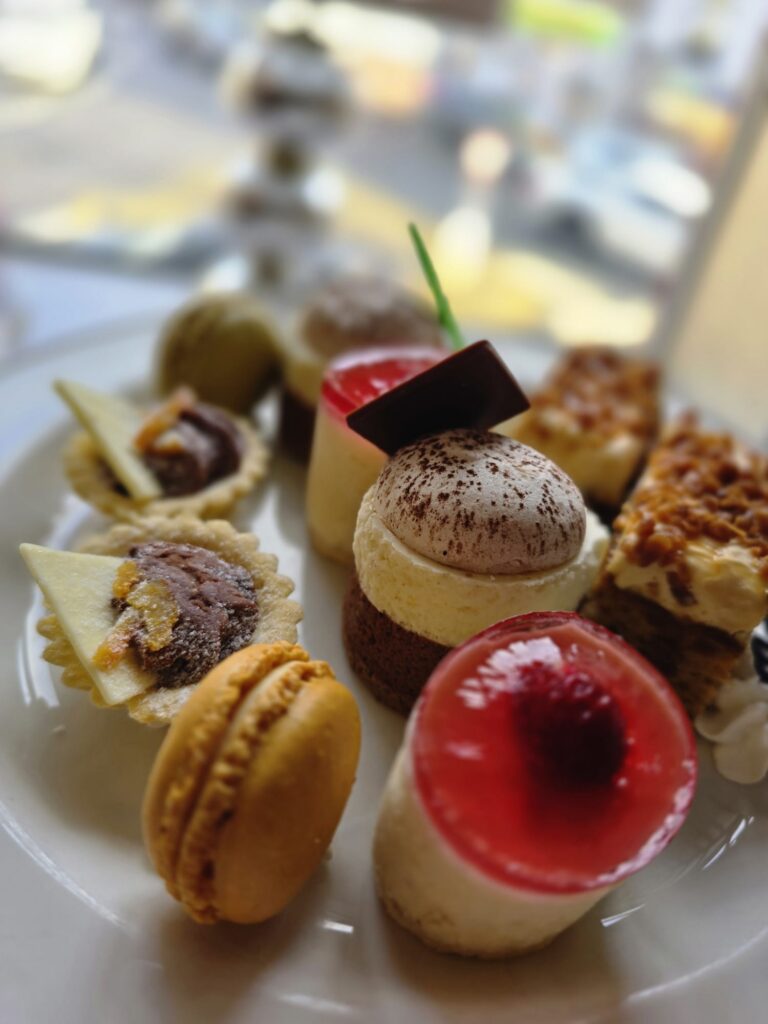 WhatsApp Image 2026-02-27 at 15.59.49 (5) A plate with an assortment of small pastries and desserts, including macarons, tarts, cakes, and mousse, arranged in a close-up view.